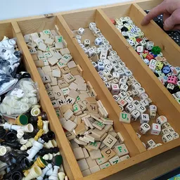 Houten sorteerkast met vakken vol verschillende spellen en speelgoed, zoals dobbelstenen, Scrabble-stenen en kleurrijke spelo