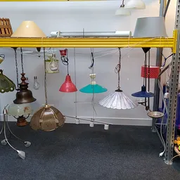 Hanglampen en lampen in verschillende kleuren en stijlen aan een gele stang uitgestald in de winkel