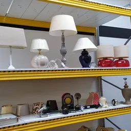 Gele stellingen met diverse lampen, servies en decoratieve huishoudartikelen.