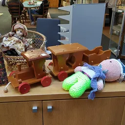 Uitgestalde kinderspeelgoed: houten trein met rode wielen, gehaakte knuffels en een pop in een rieten mand