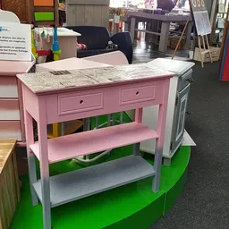 Roze houten keukeneiland met marmeren blad en twee lades, op groen platform in kringloopwinkel