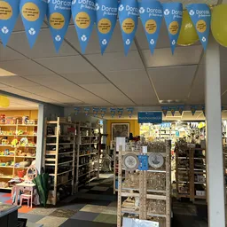 Binnenaanzicht van kringloopwinkel met stellingen, boeken, decoraties en blauwe vlaggen aan het plafond