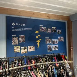Kledingrekken met tweedehands kleding en informatiebord met foto's van Dorcas projecten aan de muur