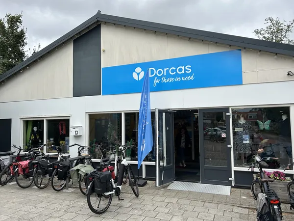 Voorgevel van Dorcas kringloopwinkel met blauwe naam, grote ramen en fietsen geparkeerd ervoor
