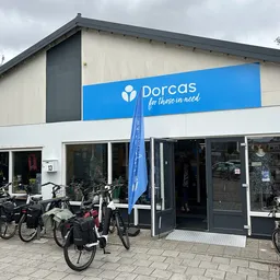 Voorgevel van Dorcas kringloopwinkel met blauwe naam, grote ramen en fietsen geparkeerd ervoor