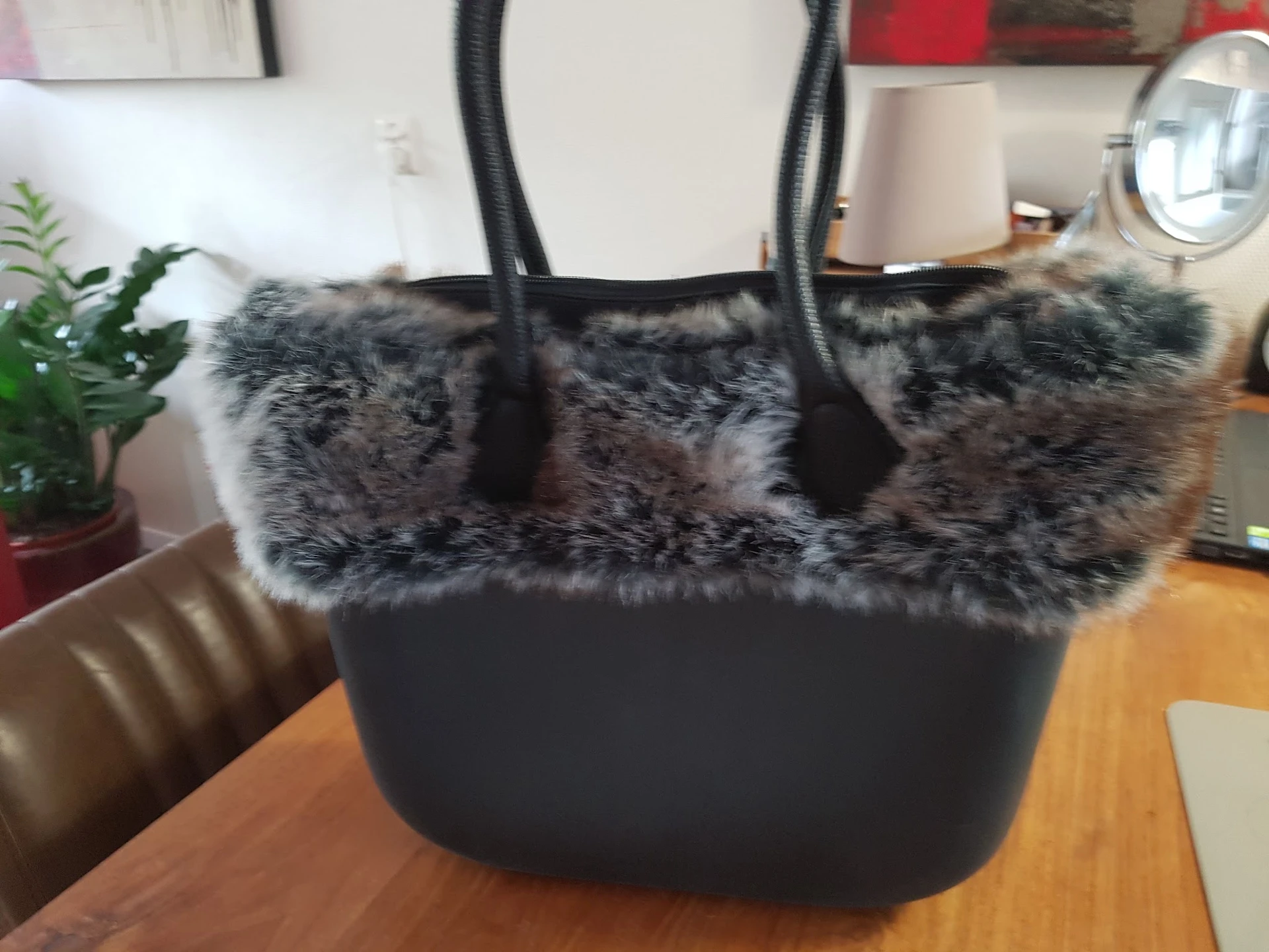 Zwarte handtas met grijze bontafwerking en zwarte hengsels, op houten tafel.