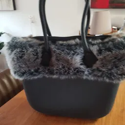 Zwarte handtas met grijze bontafwerking en zwarte hengsels, op houten tafel.
