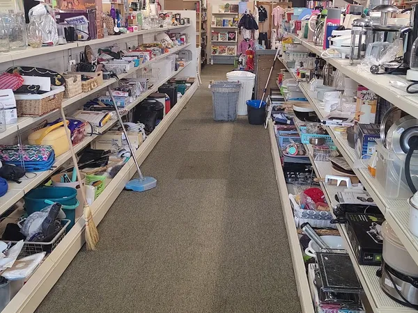 Winkelvloer met stellingen vol tweedehands spullen, kleding en huishoudartikelen aan beide zijden