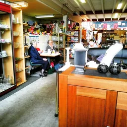 Winkelvloer van kringloopwinkel met houten toonbank, stellingen met spullen, en klanten in de winkel