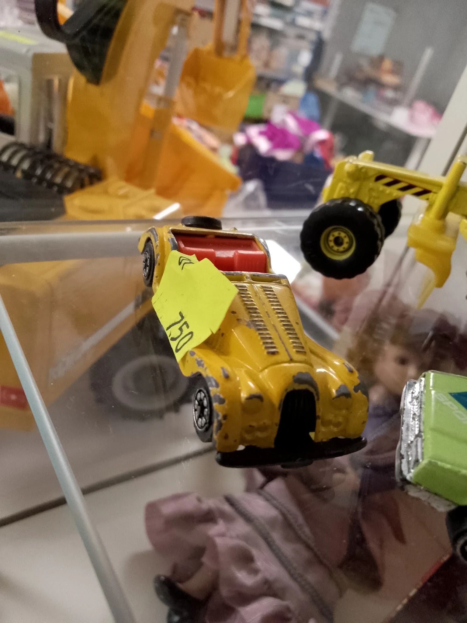 Gele speelgoedauto met geel prijskaartje tussen andere miniatuurauto's in vitrinekasten.