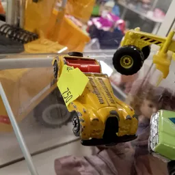 Gele speelgoedauto met geel prijskaartje tussen andere miniatuurauto's in vitrinekasten.