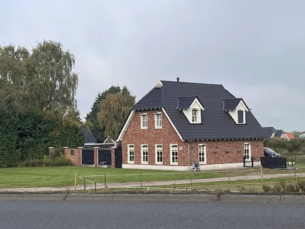 Rode bakstenen winkelpand met zwart dak aan de Noorderweg, gezien vanaf de straat met grasveld ervoor