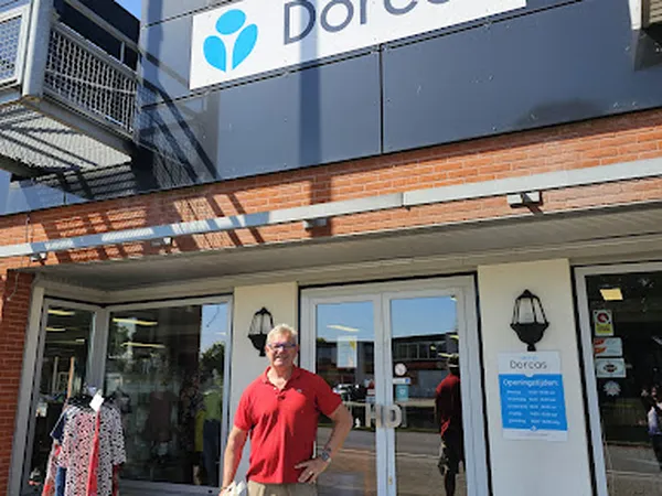 Voorgevel van kringloopwinkel Dorcas met glazen deuren, man in rood shirt ervoor, winkelnaam zichtbaar op gevel