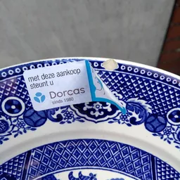 Blauw wit porselein schaaltje met Dorcas-label en Nederlandse tekst 'met deze aankoop steunt u Dorcas sinds 1980'
