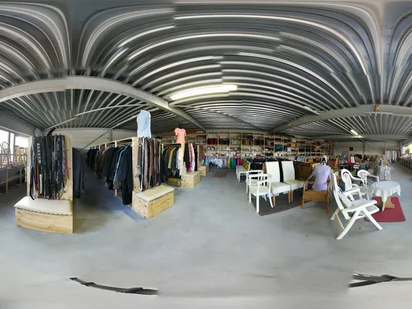Ruim winkelinterieur met stellingen, kledingrekken, witte stoelen en diverse tweedehands artikelen onder gewelfde zinkdaken