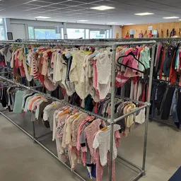 Rekken vol tweedehands kinderkleding in diverse kleuren en maten in de winkel