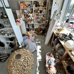 Overzicht van een volle kringloopwinkel met stellingen vol spullen, dozen op de vloer en rommelige inrichting