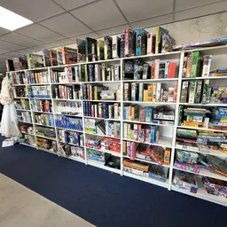 Witte stellingen volgestapeld met boeken, bordspellen en dvd's in een kringloopwinkel