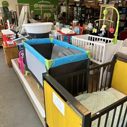 Verschillende babybedden en kindermeubels uitgestald in de winkel, waaronder witte en zwarte modellen met blauwe en gele acce