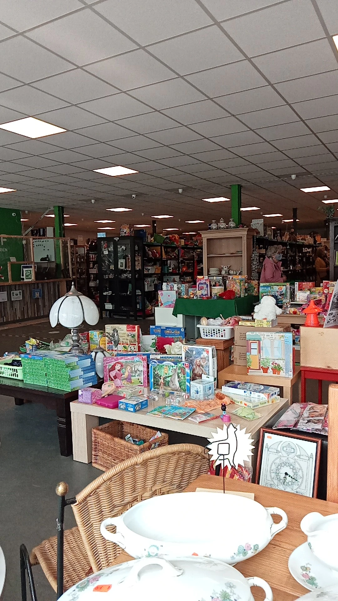 Binnenaanzicht van kringloopwinkel met speelgoed, boeken en diverse artikelen op tafels en stellingen