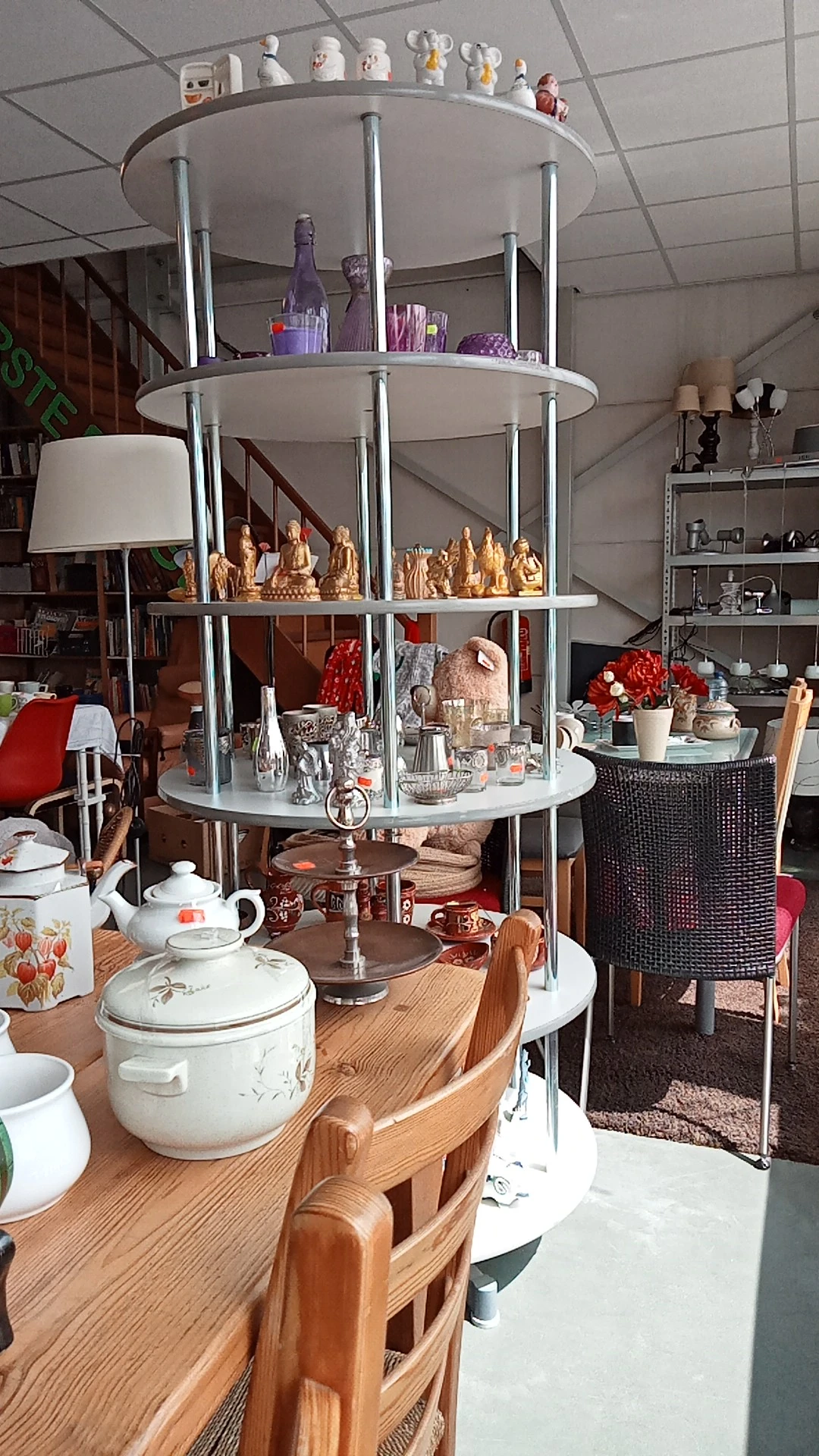 Uitgestalde decoratieve items en serviesgoed: gouden beeldjes, rode bloemen, witte porseleinen servies en diverse huishoudart