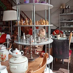Uitgestalde decoratieve items en serviesgoed: gouden beeldjes, rode bloemen, witte porseleinen servies en diverse huishoudart
