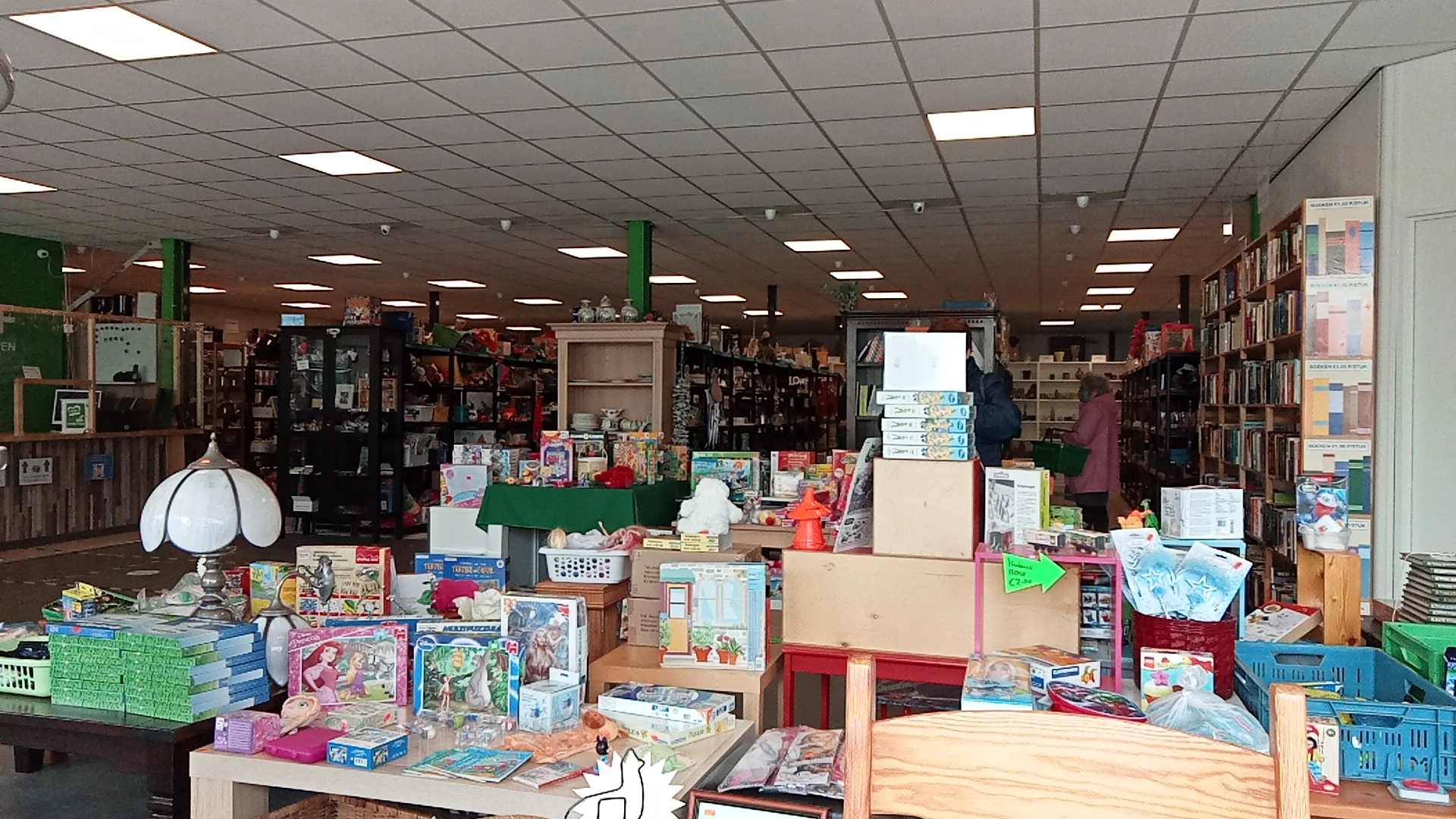 Binnenaanzicht van kringloopwinkel met stellingen, toonbanken vol boeken, speelgoed en diversen huishoudartikelen