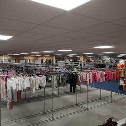 Overzicht van de winkelruimte met rekken vol tweedehands kleding, goederen op planken en een heldere plafondverlichting