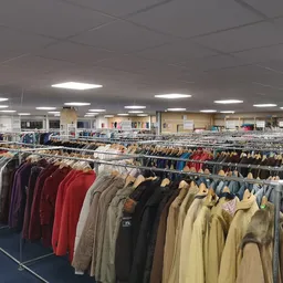 Lange rekken met tweedehands kleding in verschillende kleuren en stijlen, opgehangen aan houten hangers in een kringloopwinke