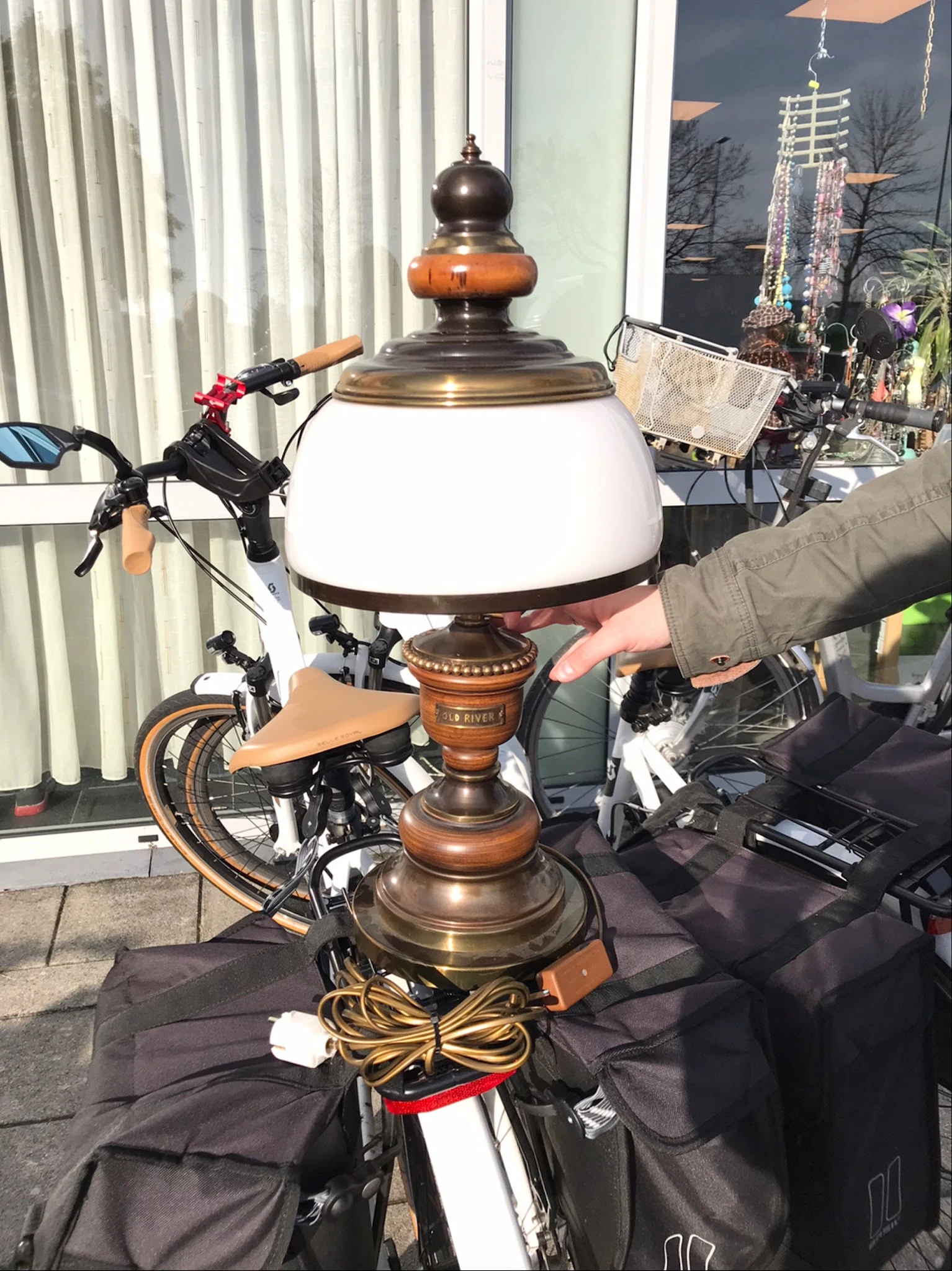Vintage staande lamp met witte melkglasbol en houten sokkel, naast een fiets