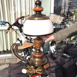 Vintage staande lamp met witte melkglasbol en houten sokkel, naast een fiets