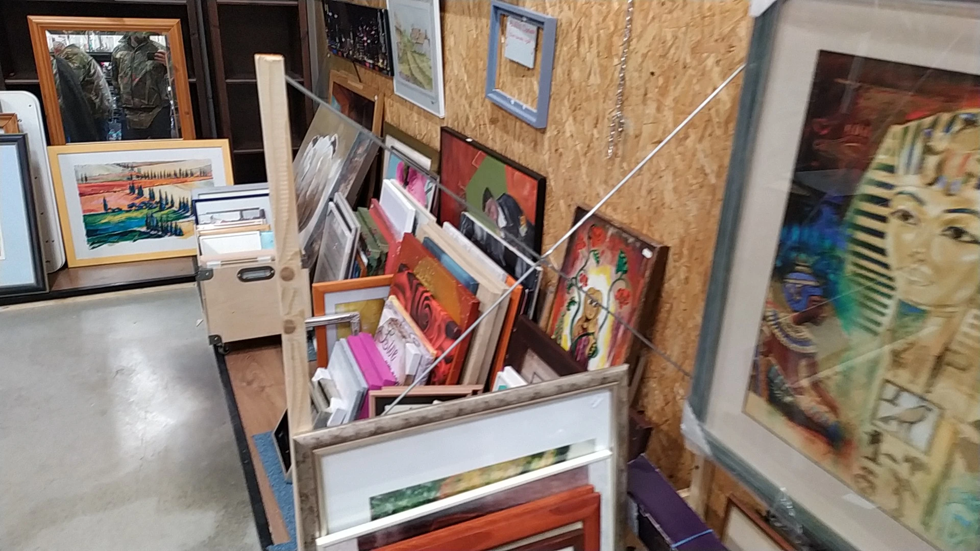 Kunstwerken en schilderijen gestapeld in en tegen een rek in de kringloopwinkel