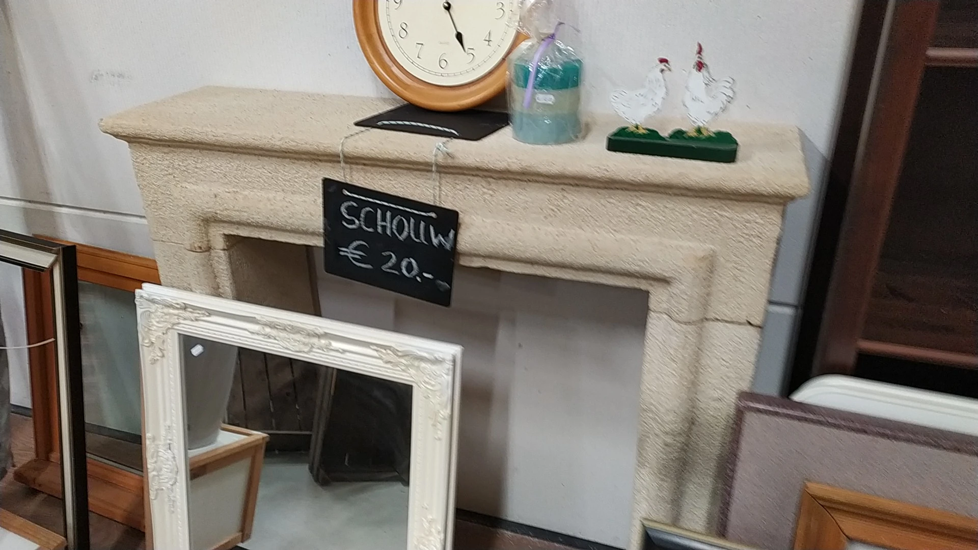 Decoratieve schouw/open haard in crèmekleur met prijskaartje van 20 euro, klok, fles en plantje erop