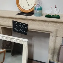 Decoratieve schouw/open haard in crèmekleur met prijskaartje van 20 euro, klok, fles en plantje erop
