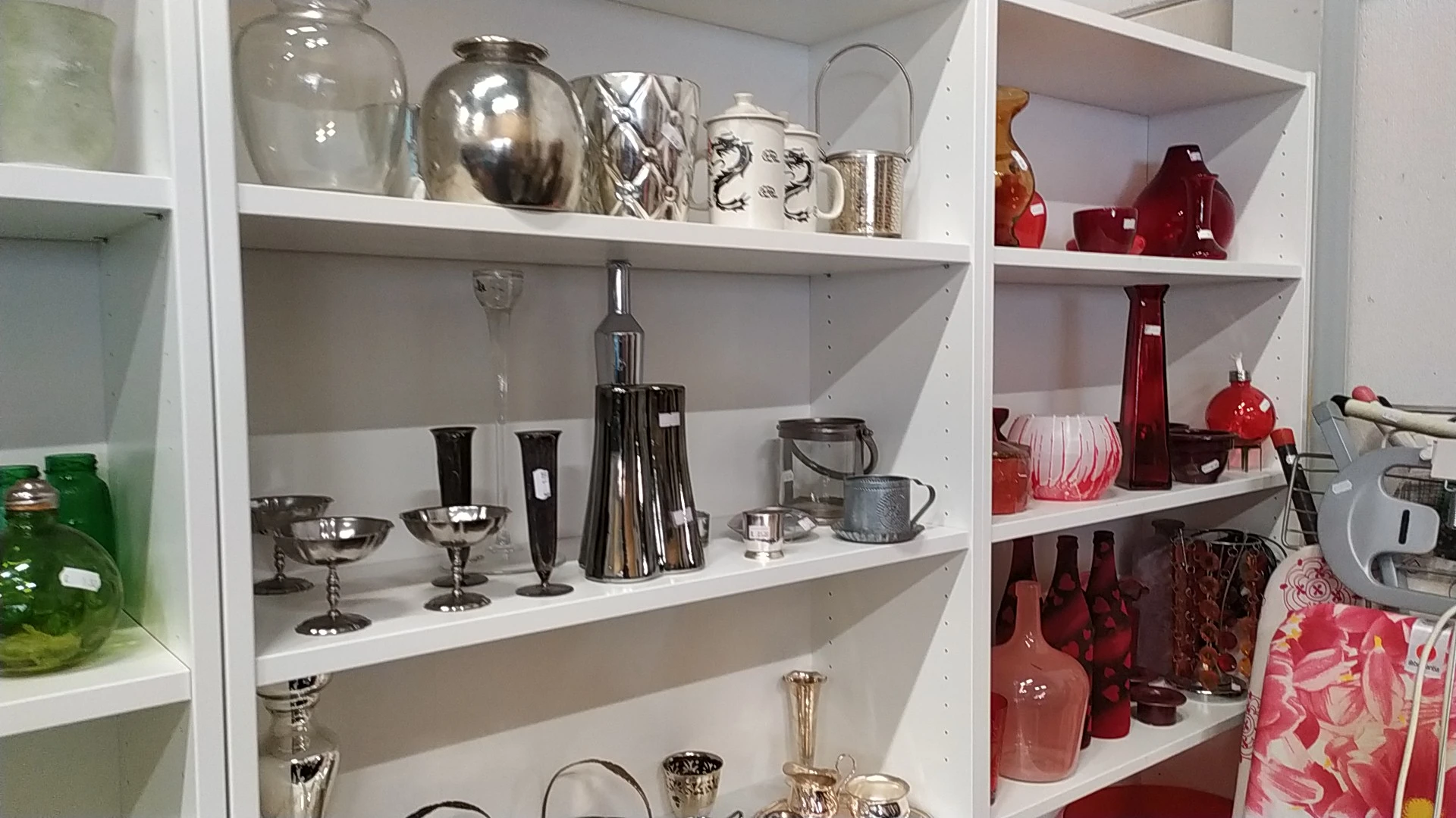 Witte kasten met zilverkleurig en rood glaswerk, vazen, kandelaars en decoratieve huishoudartikelen