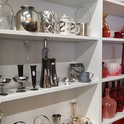 Witte kasten met zilverkleurig en rood glaswerk, vazen, kandelaars en decoratieve huishoudartikelen
