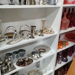 Witte stellingkast met zilverkleurig serviesgoed, kandelaars, vazen en decoratieve items op meerdere niveaus