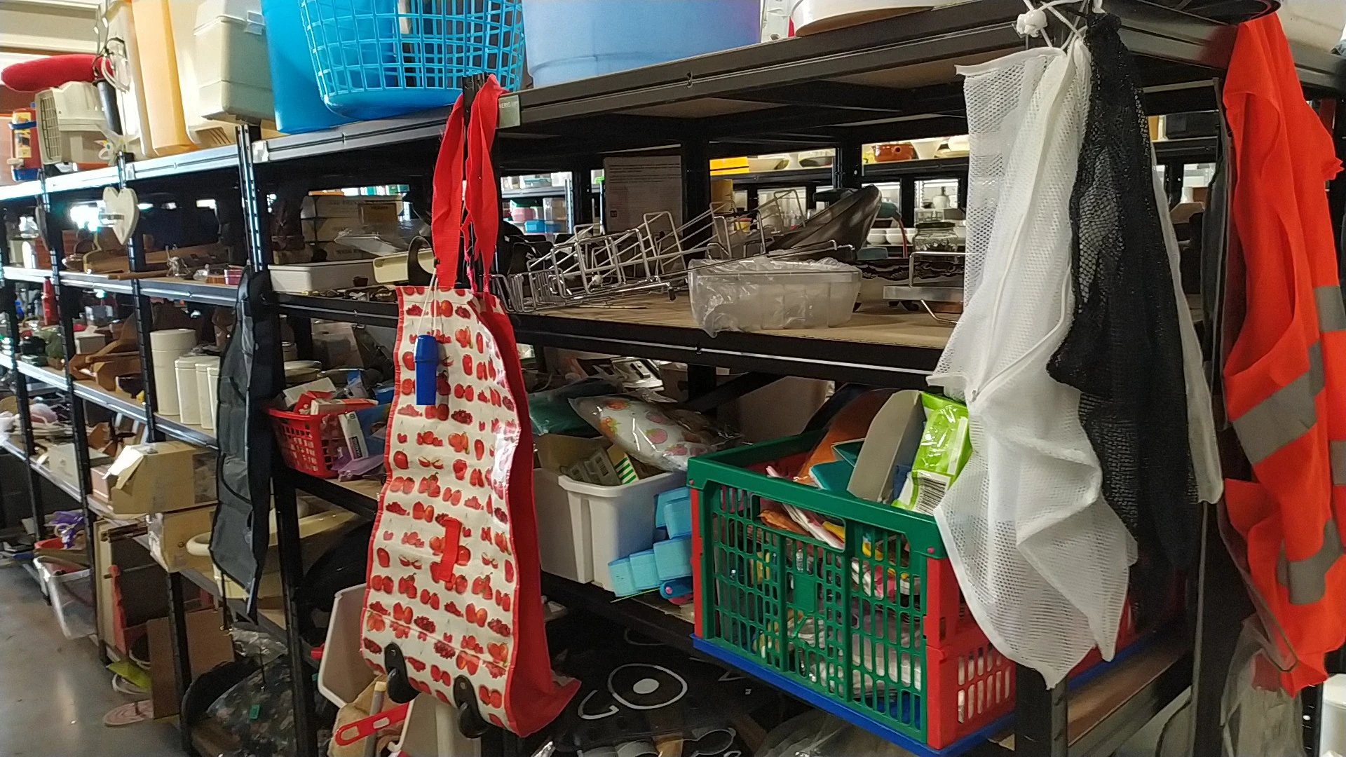 Binnenaanzicht van kringloopwinkel met stellingen, kratjes, doeken en diverse spullen op planken.