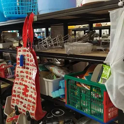 Binnenaanzicht van kringloopwinkel met stellingen, kratjes, doeken en diverse spullen op planken.