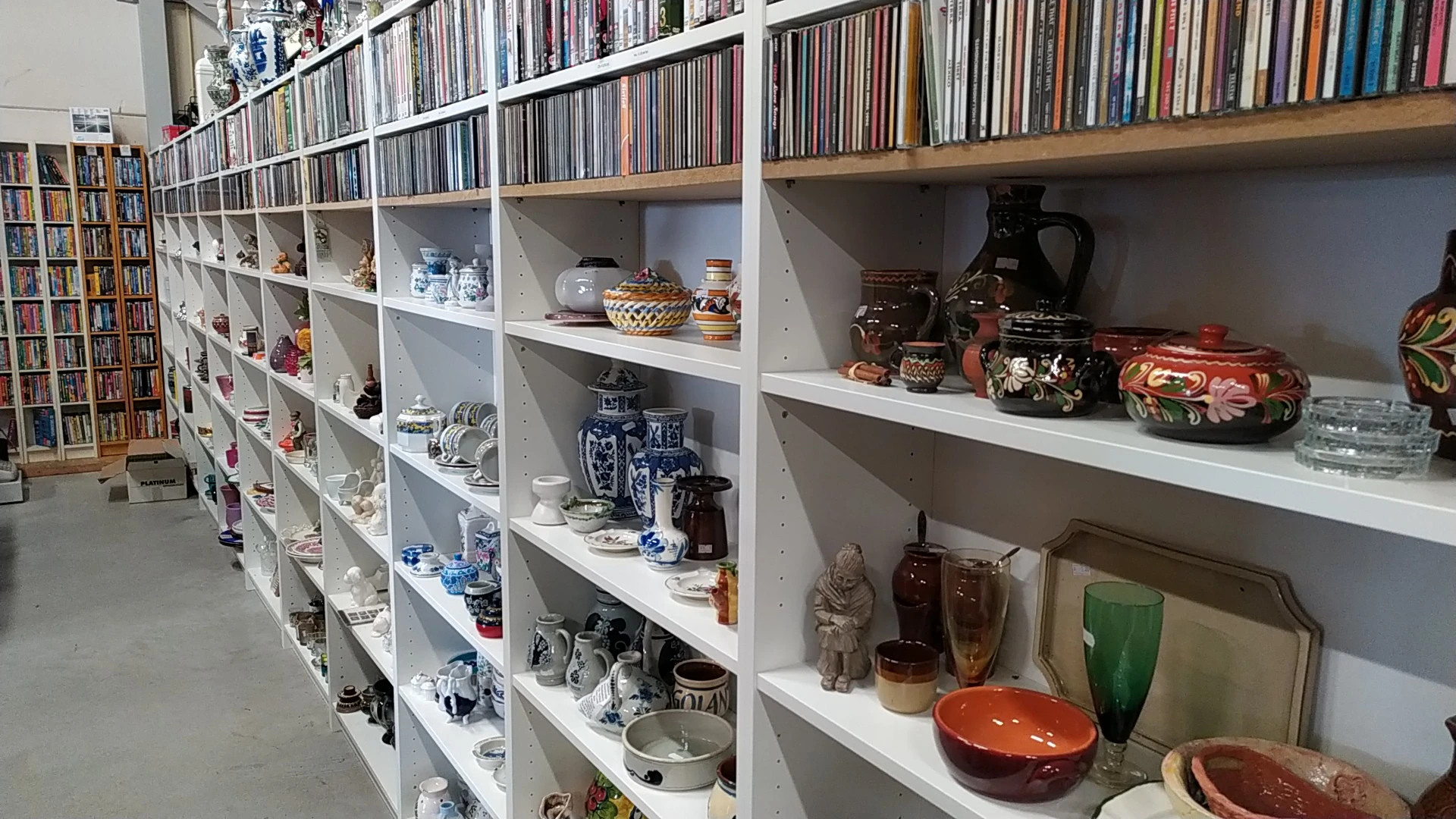 Witte stellingen met tweedehands serviesgoed, decoratieve objecten, cd's en keramiek netjes uitgestald