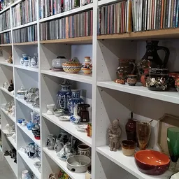 Witte stellingen met tweedehands serviesgoed, decoratieve objecten, cd's en keramiek netjes uitgestald