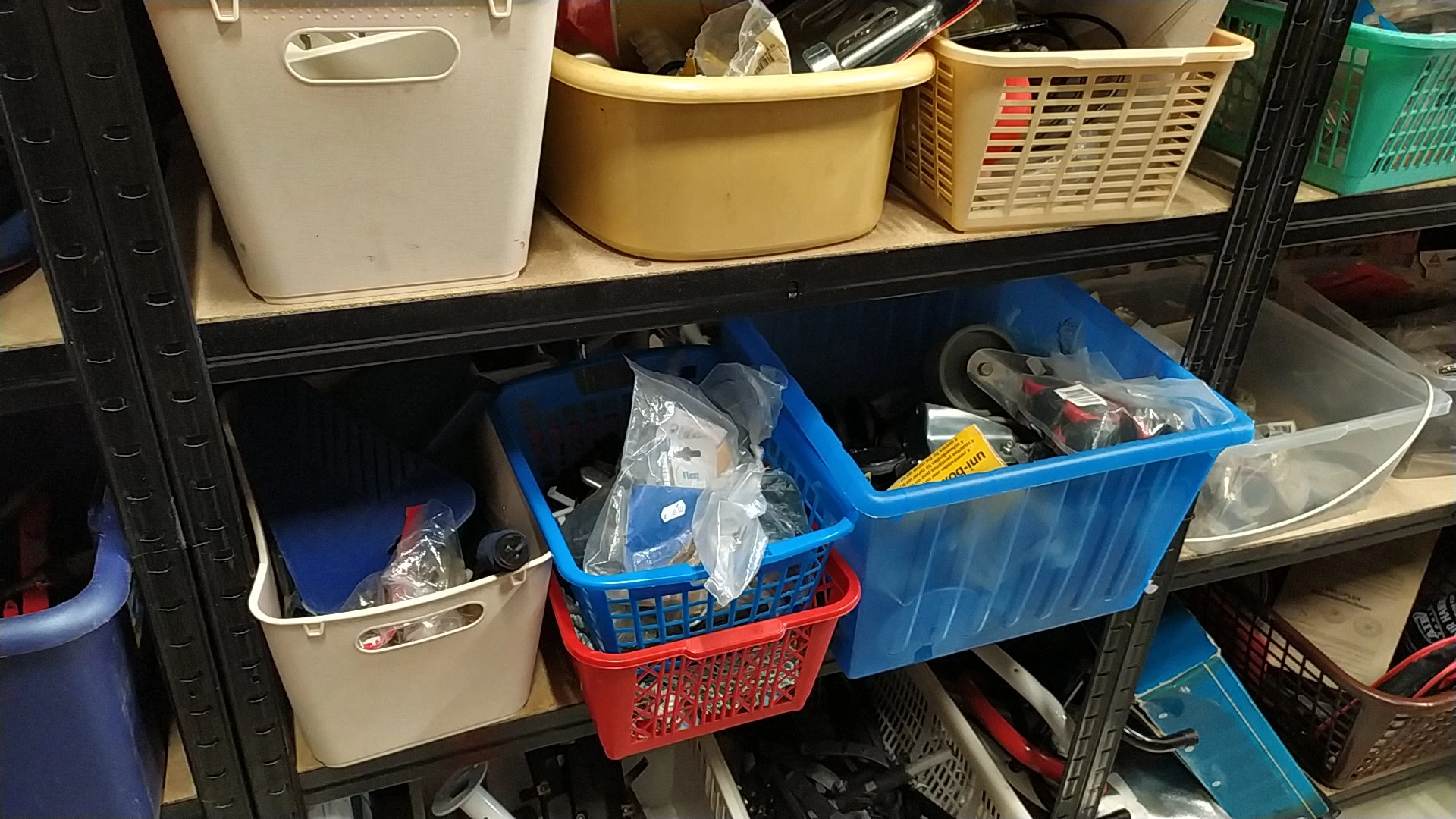 Stellingen met blauwe en rode plastic bakken en beige opbergmanden gevuld met diverse spullen in een kringloopwinkel