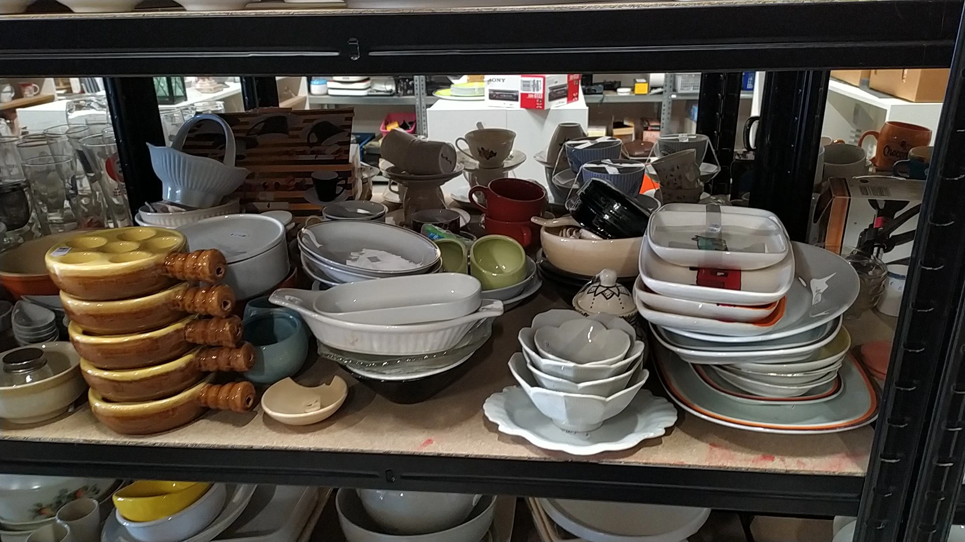 Uitgestalde serviesgoed en kookgerei op een winkelplank in een kringloopwinkel