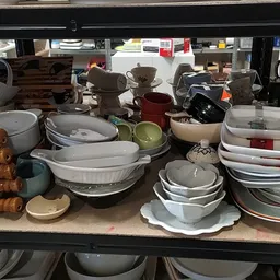 Uitgestalde serviesgoed en kookgerei op een winkelplank in een kringloopwinkel