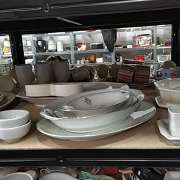 Uitgestalde serviesgoed: witte en grijze borden, schalen en kommen op een toonbank in de kringloopwinkel