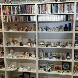 Witte boekenkast met dvd's, cd's bovenin en verzameling decoratieve items zoals beeldjes, servies en glazen op de planken ero