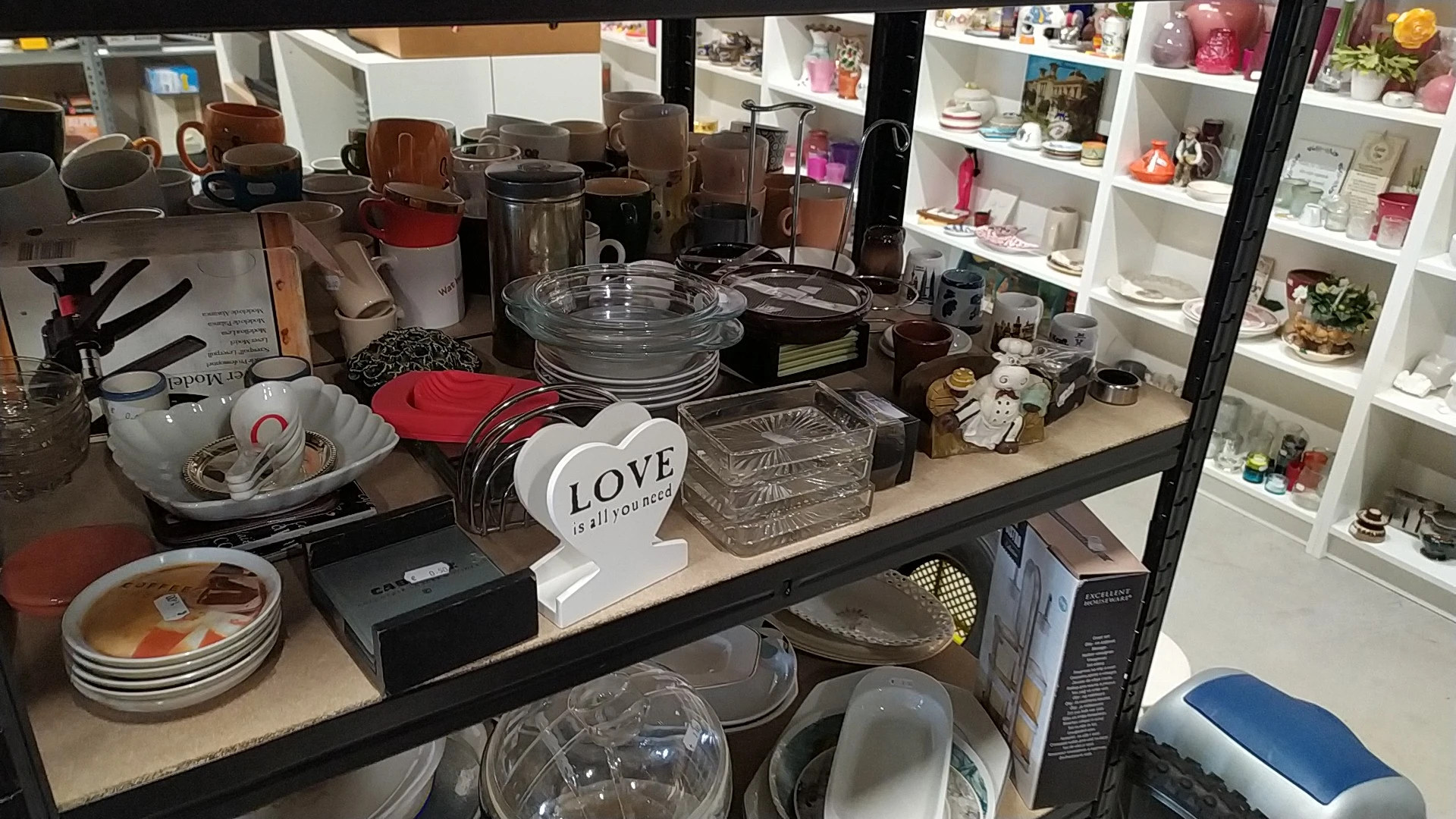 Tafel vol huishoudspullen: bordenstapels, glazen schalen, rode servethouder en witte 'Love' decoratie