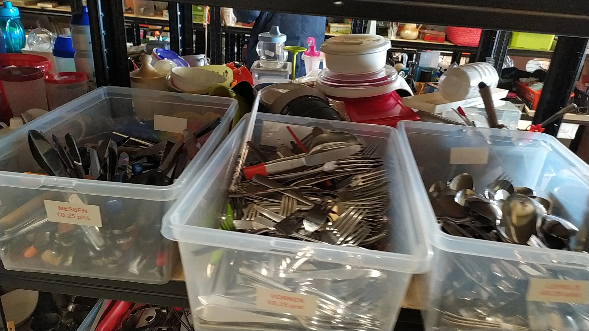 Plastic bakken met bestek, servies en huishoudelijke spullen in de kringloopwinkel