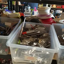 Plastic bakken met bestek, servies en huishoudelijke spullen in de kringloopwinkel