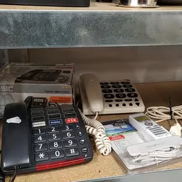 Tweedehandstelefoons en apparaten op een plank, waaronder een grote toetsentelefoon en een nummerpaneel